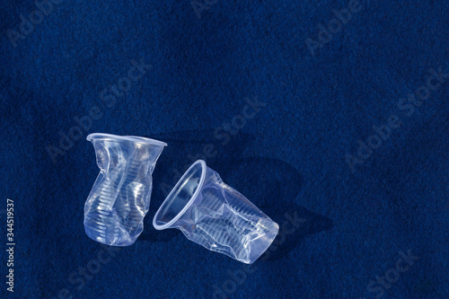 Two smashed transparent plastic cups on a blue background with copy space