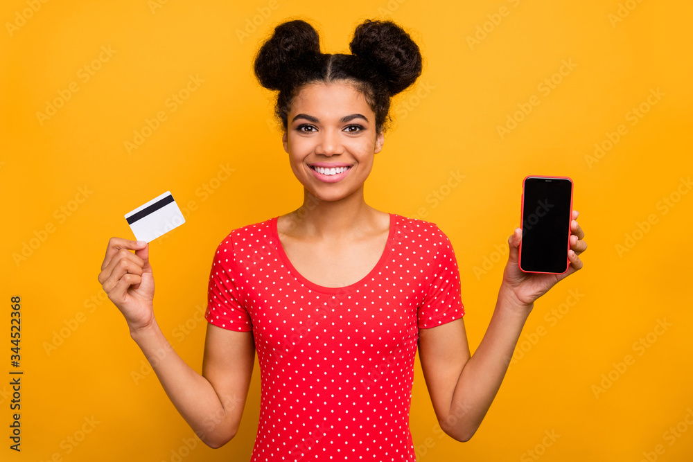 Positive cheerful afro american girl hipster promoter hold cellphone debit card recommend easy banking online payment wear red dotted t-shirt isolated over bright shine color background Positive cheerful afro american girl hipster promoter hold cellphone debit card recommend easy banking online payment wear red dotted t-shirt isolated over bright shine color background