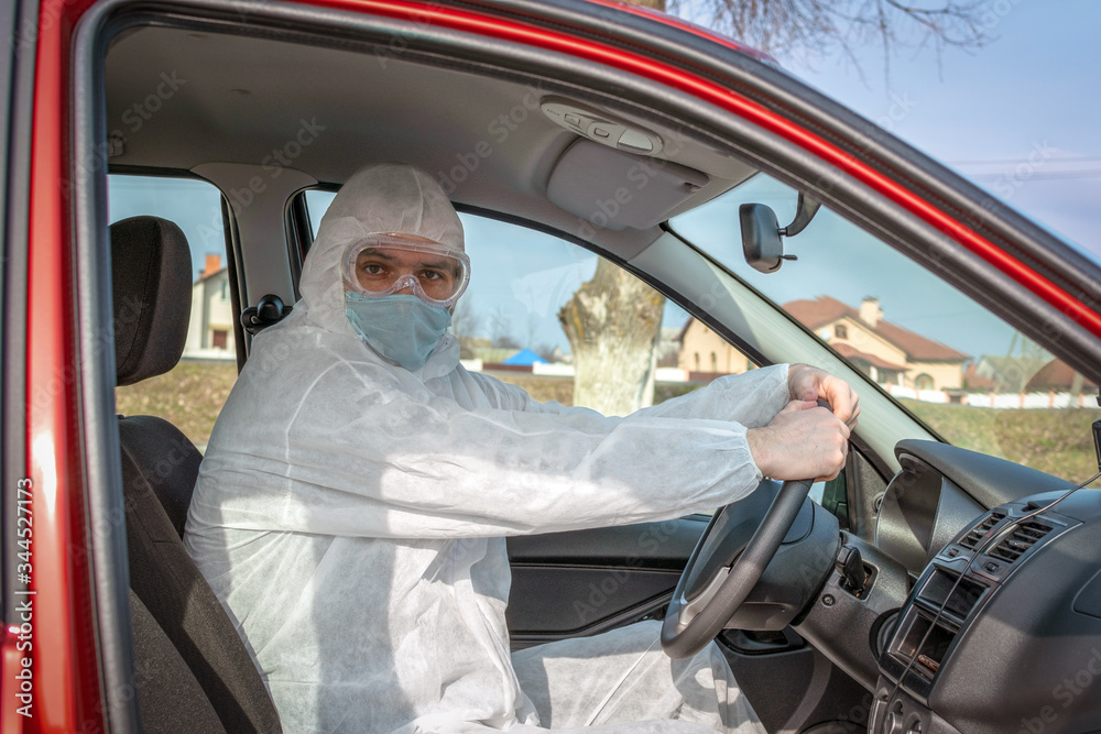 man sits in a car in a protective suit, goggles and a medical mask for respiratory protection