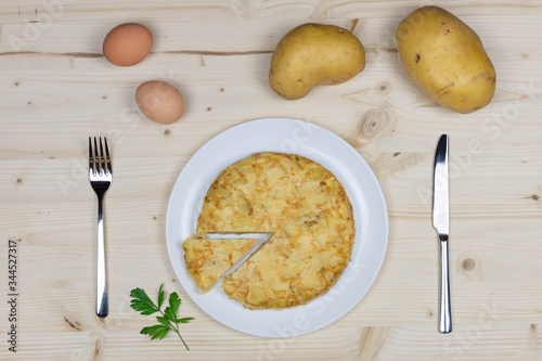 Potato omelette typical Spanish dish called tortilla de patatas in Spanish. with potatoes and eggs from above on a wooden table