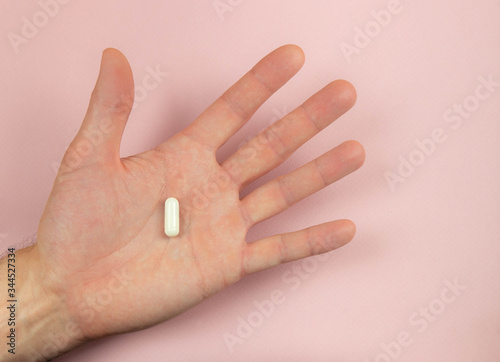 Hand holding a pill on a pink background. Minimalism. Copy space Selective focus