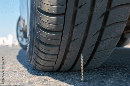 puncture wheel concept. the self-tapping screw lies on asphalt under a car wheel