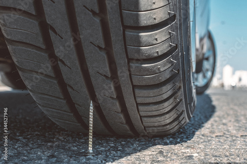 
puncture wheel concept. the self-tapping screw lies on asphalt under a car wheel