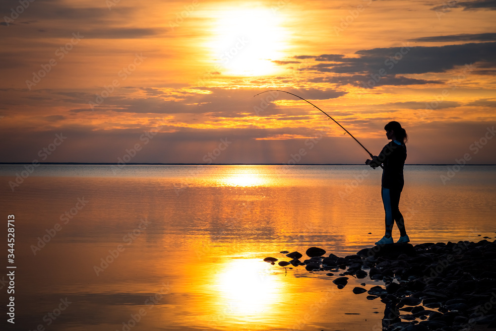 Woman fishing on Fishing rod spinning at sunset background.