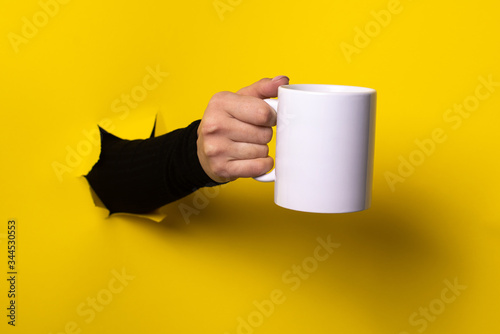 Hot drink concept.Hand holding mug from a torn hole in yellow paper