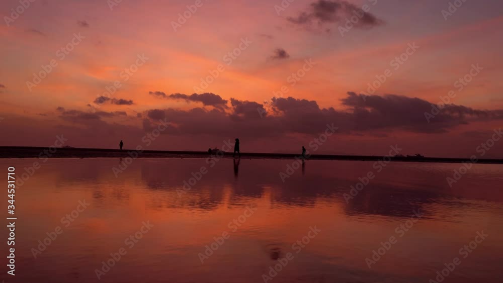 Incredibly beautiful fiery red sunset on the ocean at low tide. Silhouettes People walk along the shore looking at the bottom of the ocean Incredibly beautiful fiery red sunset on the ocean at low tide. Silhouettes People walk along the shore looking at the bottom of the ocean