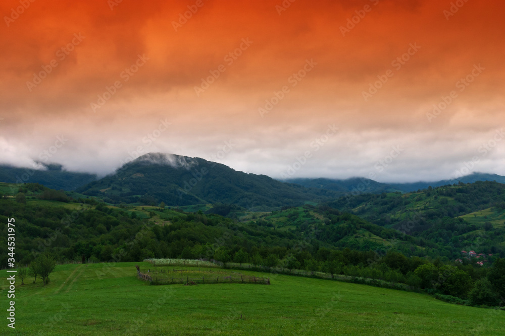 Mountain landscape with red sky and green field.