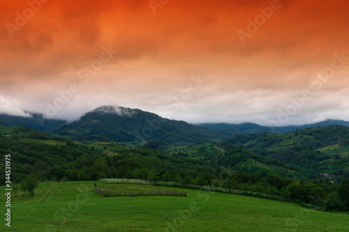 Mountain landscape with red sky and green field.