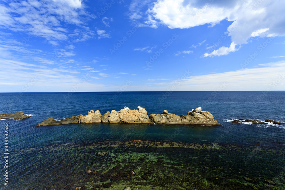 Horizontal seascape with white clouds. Quiet blue sea and rocky island.