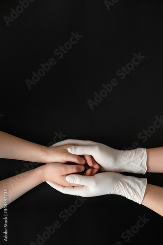 Doctor's hands in white gloves holding child's hands. Medical banner with copy space on black background. Care concept.