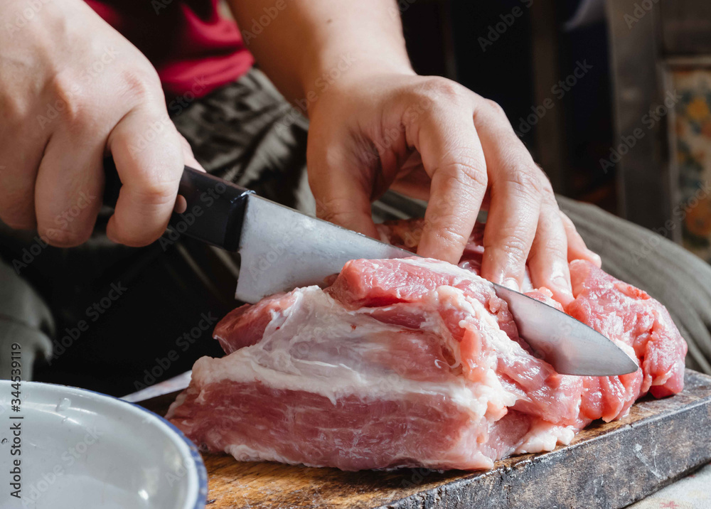 The hand of a young woman slicing pork into small pieces in order to cook different types of food, home cooking. Concept