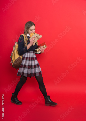 Schoolgirl in uniform with a backpack comes and eats at the same time, she keeps books, long braids