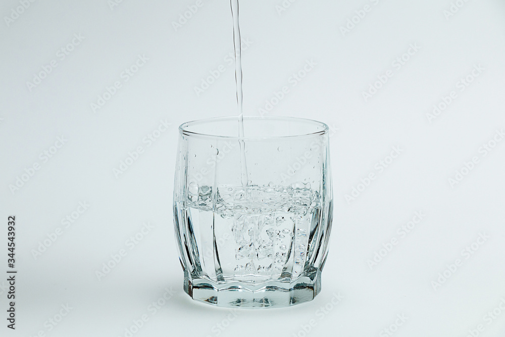 Water is poured into a transparent glass on a white background Water is poured into a transparent glass on a white background