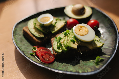 Delicious breakfast at home. Sandwich with fresh sliced avocado above rye bread with cherry tomatoes and boiled egg on green plate