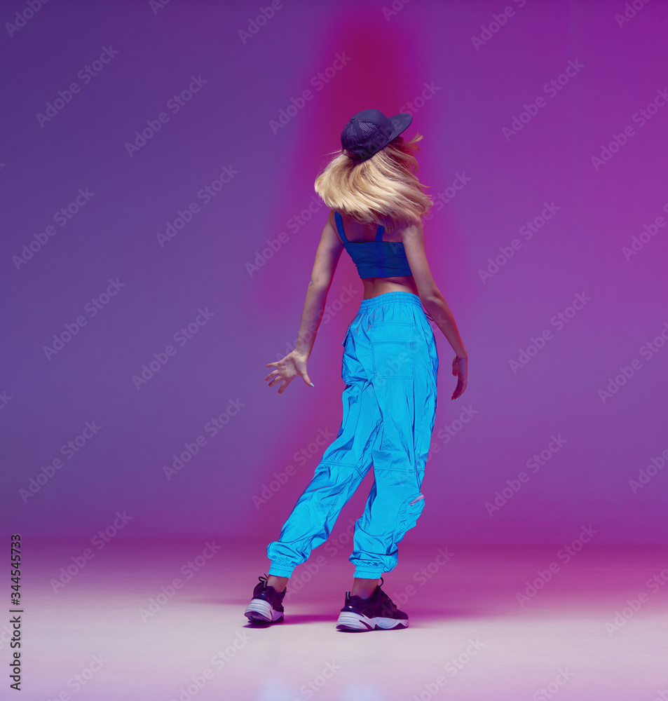 Cute teen girl dancing hip hop in reflective pants, baseball cap, in a  Studio with neon lighting. Dance color poster. Stock Photo