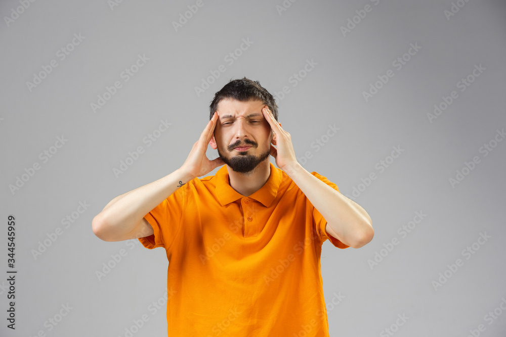 Young caucasian man suffers from headache, feels sick, ill and weakness isolted on gray studio background. Symptoms of desease or unhealthy lifestyle. Sickness, ilness, sad and upset. Copyspace. Young caucasian man suffers from headache, feels sick, ill and weakness isolted on gray studio background. Symptoms of desease or unhealthy lifestyle. Sickness, ilness, sad and upset. Copyspace.