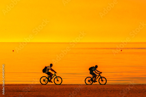 Biker silhouette riding along beach at sunset on bike Sporty company group of friends on bicycle outdoors Success achievement accomplishment and winning concept with cyclist mountain biking Copyspace