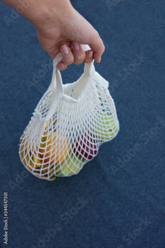 Hand holding mesh shopping bag with fruits on the gtay background, top view vertical photo photo