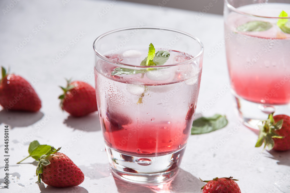 Glasses of strawberry water with strawberries, ice and fresh mint leaves on concrete background stone strong light with glass shadows. Copy space. Close up Glasses of strawberry water with strawberries, ice and fresh mint leaves on concrete background stone strong light with glass shadows. Copy space. Close up