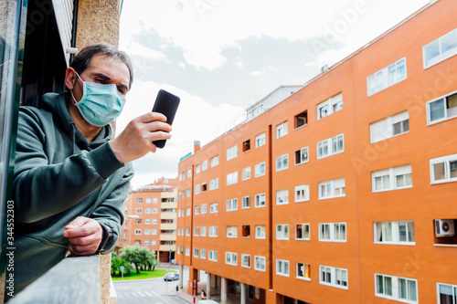 sick man covid-19 virus with mask peeking out the window using a smartphone