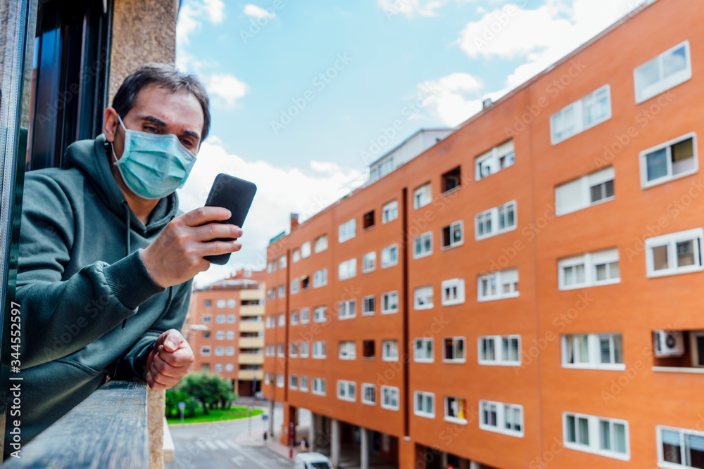 sick man covid-19 virus with mask peeking out the window using a smartphone sick man covid-19 virus with mask peeking out the window using a smartphone