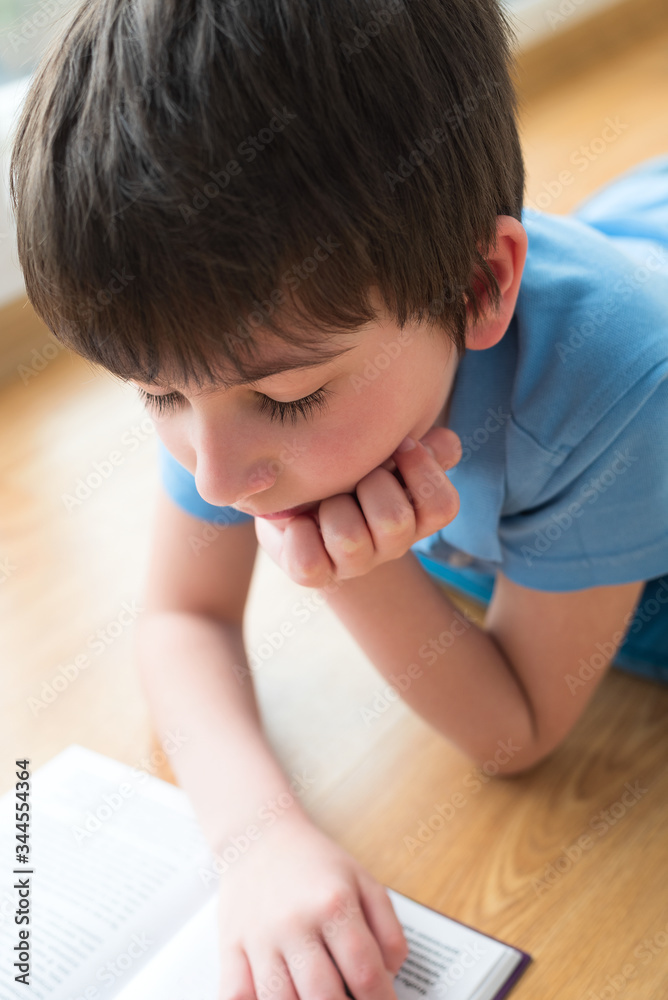 Nine years old child reading book lying on pillow. Soft focus. Quarantine and online school concept Nine years old child reading book lying on pillow. Soft focus. Quarantine and online school concept