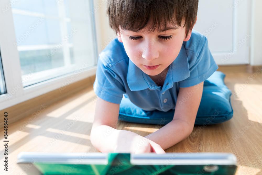 Nine years old child using tablet lying on pillow. Soft focus. Quarantine and online school concept Nine years old child using tablet lying on pillow. Soft focus. Quarantine and online school concept