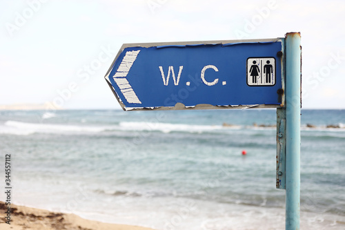 direction to the toilet on the beach. WC - inscription on signboard toilet hanging on a pole  a sea and sky background.