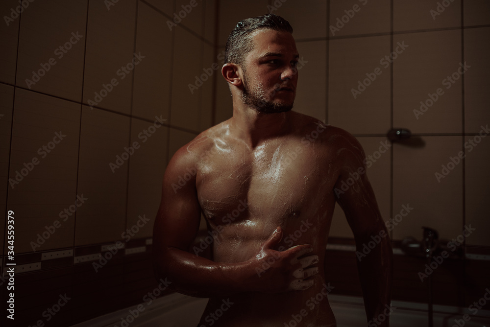 Athletic good looking and attractive man with muscular body standing under running water in shower room