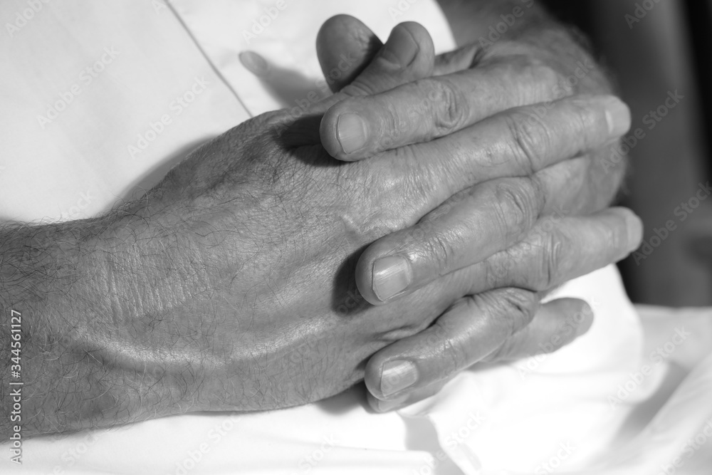 folded hands of an elderly man in black and white