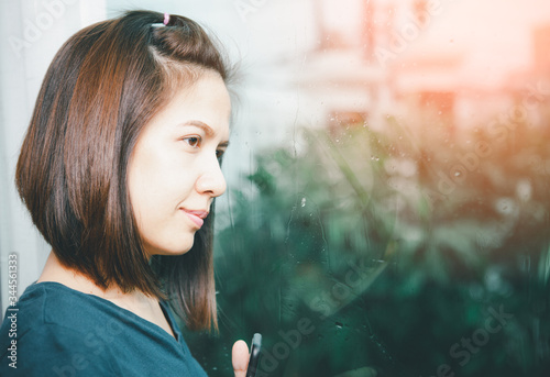 Beautiful Asian woman wearing a blue shirt, lonely mood when it rains, with reflections in the mirror.