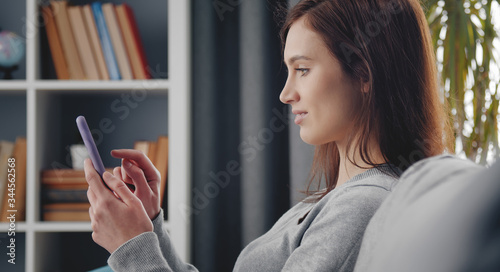 Photos Profile of young dark-haired woman using cellphone sitting on sofa at home
