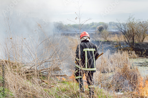 Raging forest spring fires. Burning dry grass, reed along lake. Grass is burning in meadow. Ecological catastrophy. Fire and smoke destroy all life. Firefighters extinguish Big fire. Lot of smoke photo