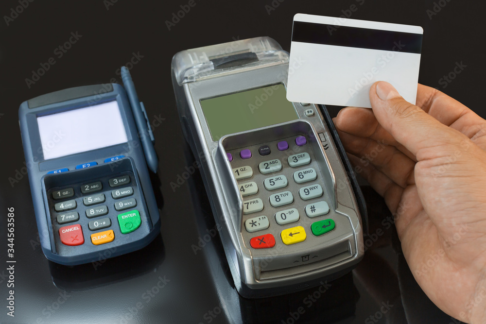 A male hand holds a payment card above the payment terminal. A male hand holds a payment card above the payment terminal.