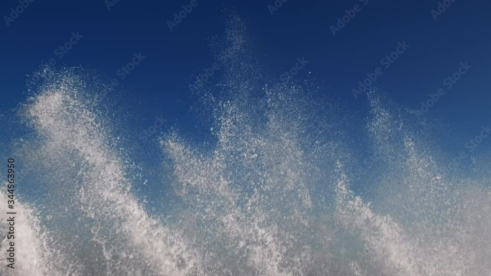 Splashes large strong waves on pier against background of bright blue sky on spring sunny day slow motion. Approaching wave with splashes of water. Strength and power of breaking wave on pier. Splash