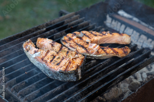 two large pieces of grilled salmon steak lie on a barbecue grill outdoor