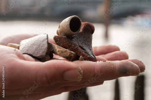 Mudlark Findings: A man's hand holds an old broken clay pipe bowl and other pieces of the past he has found while mudlarking on the River Thames photo
