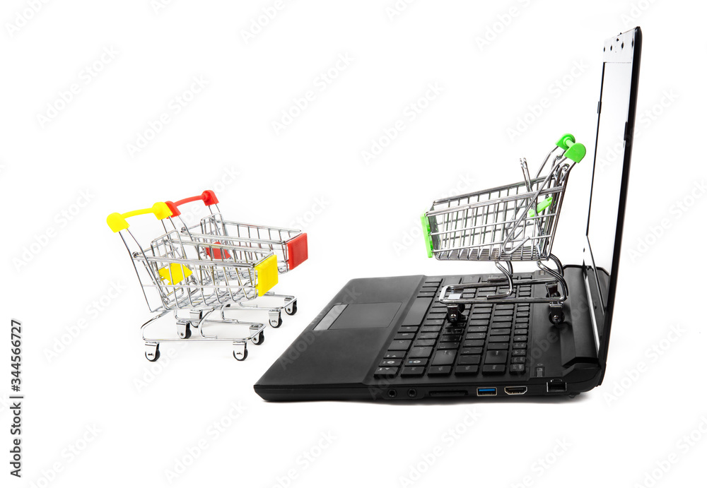 Three empty miniature shopping carts stand close to a black laptop isolated on white. E-commerce concept.