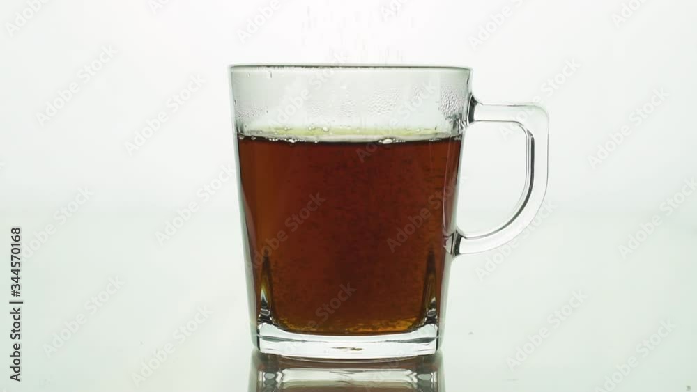 Sugar adding to transparent glass mug with black tea isolated on white background slow motion close up. Sugar adding to transparent glass mug with black tea isolated on white background slow motion close up.
