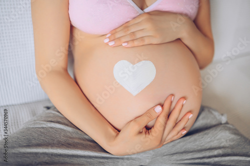 Wallpaper Mural Close up unrecognizable pregnant woman holding holding hands over her big belly with drawn white heart sign. Baby inside. Pregnancy, motherhood, unborn and expectation concept. Copy space for text  Torontodigital.ca