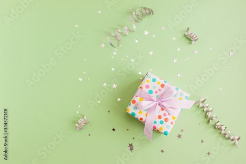 Polka dot gift box on a green background decorated with silver confetti and sepentine. Holiday and magic concept.