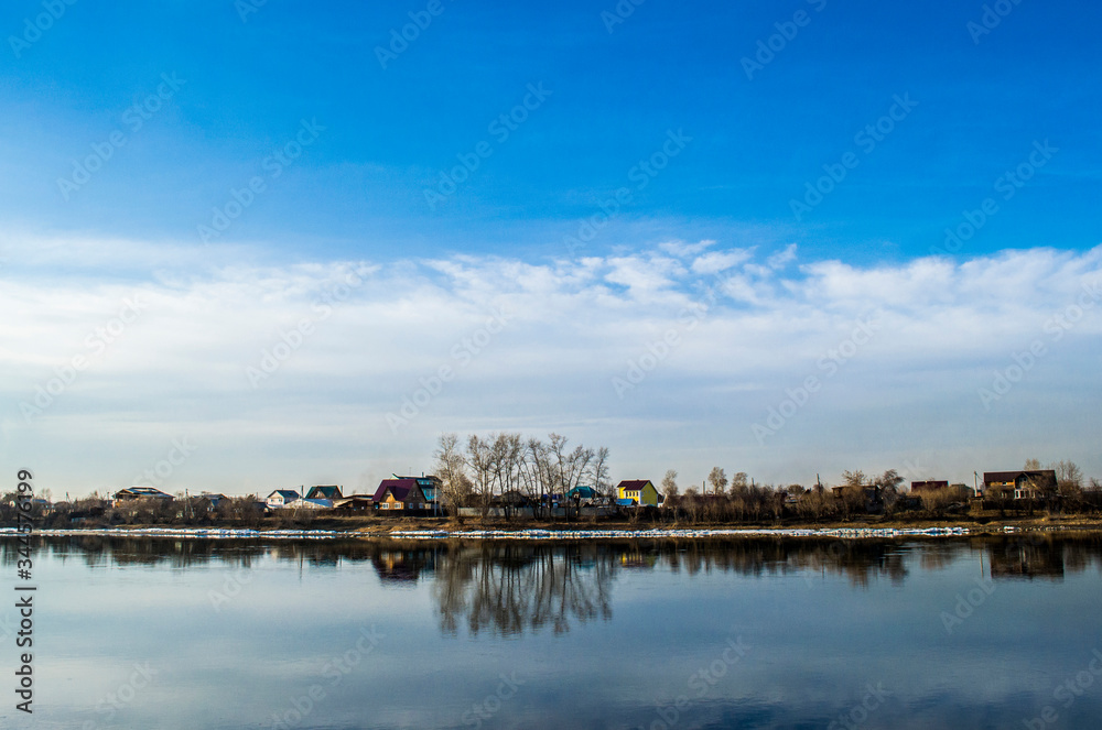 Horizon dividing a blue sky with clouds and a river with reflection of the sky and houses
