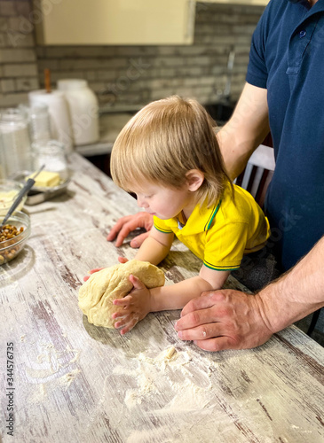 A fair-skinned little child with his father / grandfather prepares sweet rolls filled with cottage cheese and raisins in the kitchen at home. A step-by-step cooking process.Defocus light background.