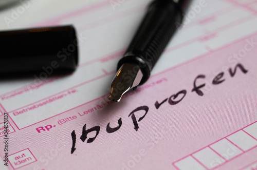 Macro closeup of isolated pink prescription note, handwritten word ibuprofen with ink pen (Focus on tip of pencil)
