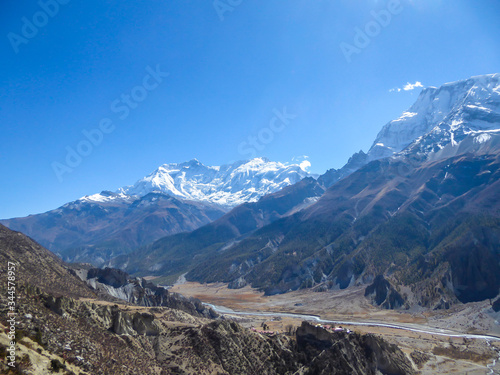 A panoramic view on Manang valley from Praken Gompa, Nepal. High Himalayan ranges around. There is a small torrent in the valley. Snow capped peaks of Annapurna Chain. Harsh landscape. © Chris
