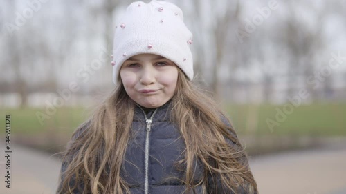 Close-up face of funny little girl making faces. Portrait of brunette Caucasian kid grimacing on sunny spring day in park. Leisure outdoors, lifestyle, fun.