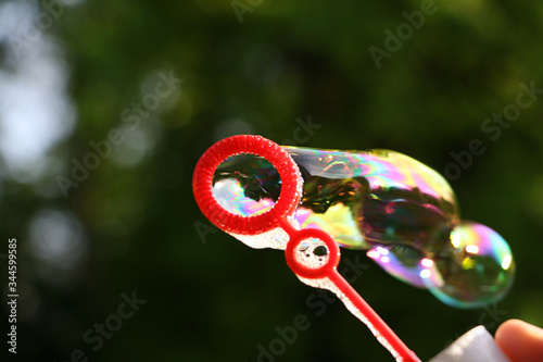 Plastic bottle with blowing colorful soap bubbles.Close up photography with many bubbles,foliage background.Summer backdrop.Multicolored bubbles.