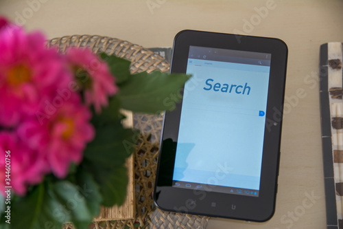 Tablet with the word search  on a table next to a flower pot. Technology