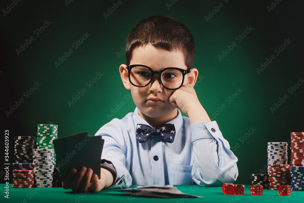 Little kid playing poker in a casino. Studio concept on blue background Little kid playing poker in a casino. Studio concept on blue background