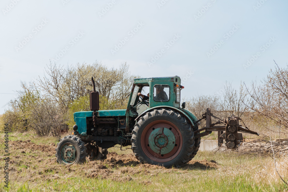 An old blue tractor plows a field and cultivates the soil. Agriculture An old blue tractor plows a field and cultivates the soil. Agriculture